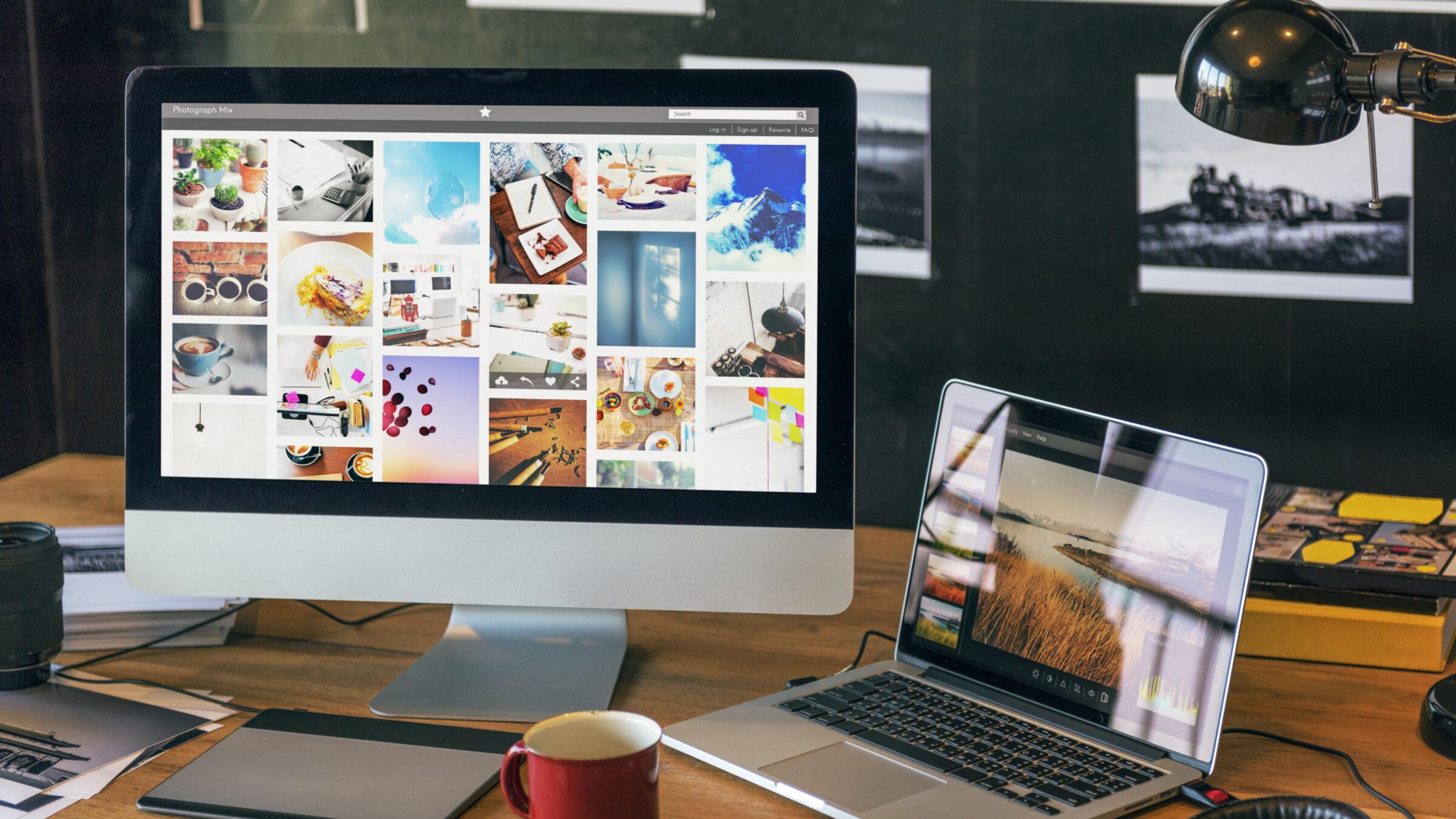 A desk with a monitor and laptop displaying photo galleries